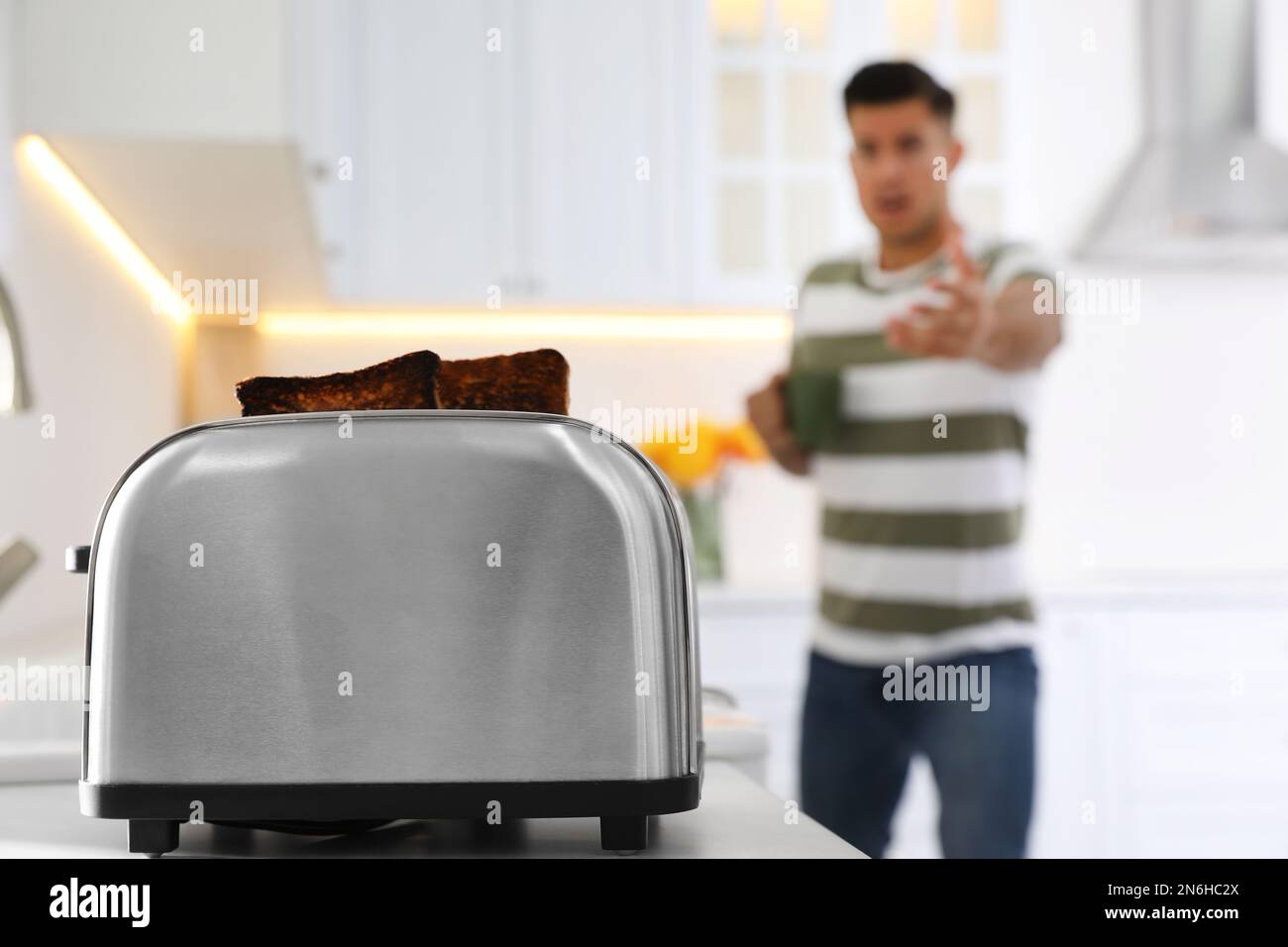 Emotivo uomo preparare la colazione in cucina, concentrarsi sul tostapane con fette di pane bruciato Foto Stock
