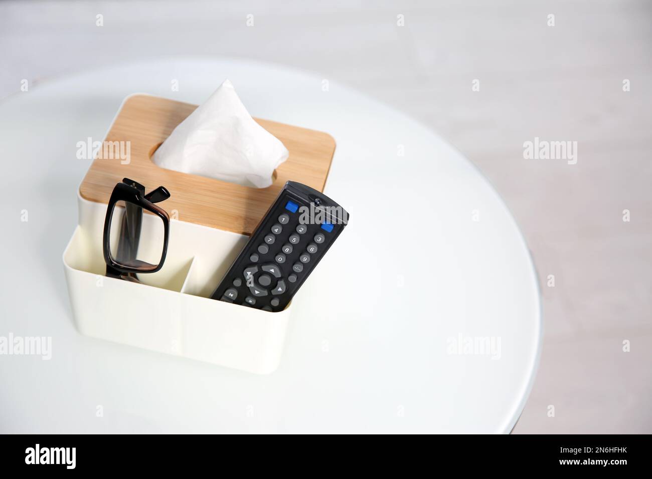 Scatola con fazzolettini di carta, occhiali e telecomando TV su tavolo bianco. Spazio per il testo Foto Stock