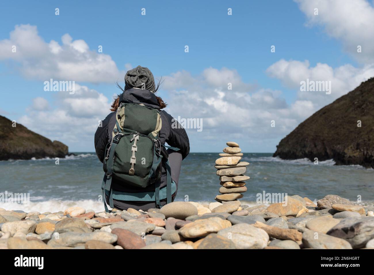 Una donna che si siede da sola e si affaccia sul mare su una spiaggia di ciottoli in Galles. Foto Stock