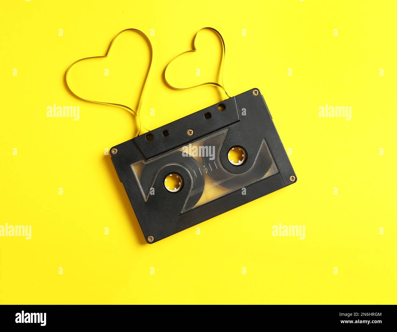 Cassetta musicale e cuori realizzati con nastro su sfondo giallo, vista dall'alto. Ascoltare la canzone d'amore Foto Stock