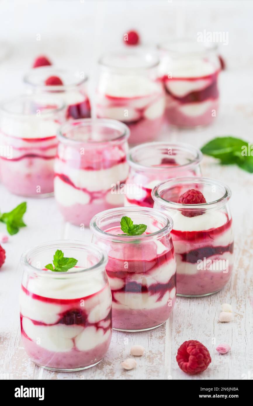 Dessert di quark fruttato con lamponi in piccoli bicchieri e cioccolato o croccante guarnizione in fila, verticale Foto Stock