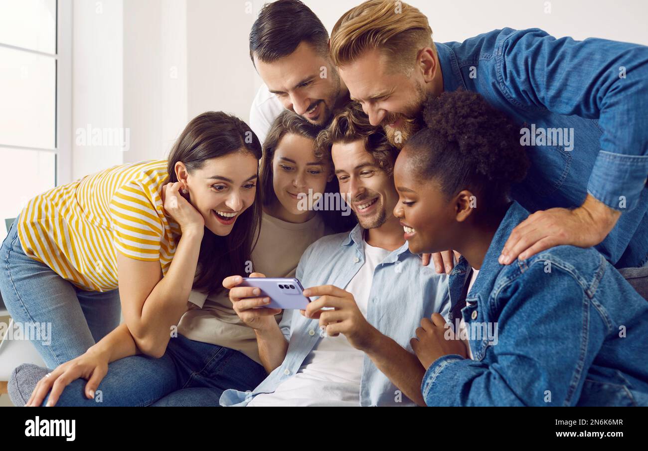 Foto di gruppo di amici felici e diversi che guardano qualcosa sul telefono cellulare insieme Foto Stock