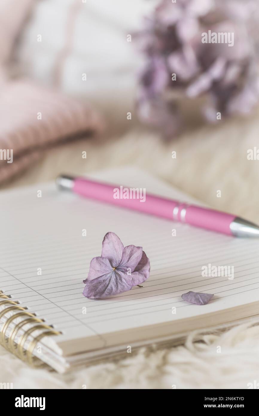 Accogliente scena di pausa caffè su una pelliccia bianca con notebook e penna, tazza e tessuto di lana, colori crema e lilla, verticale Foto Stock