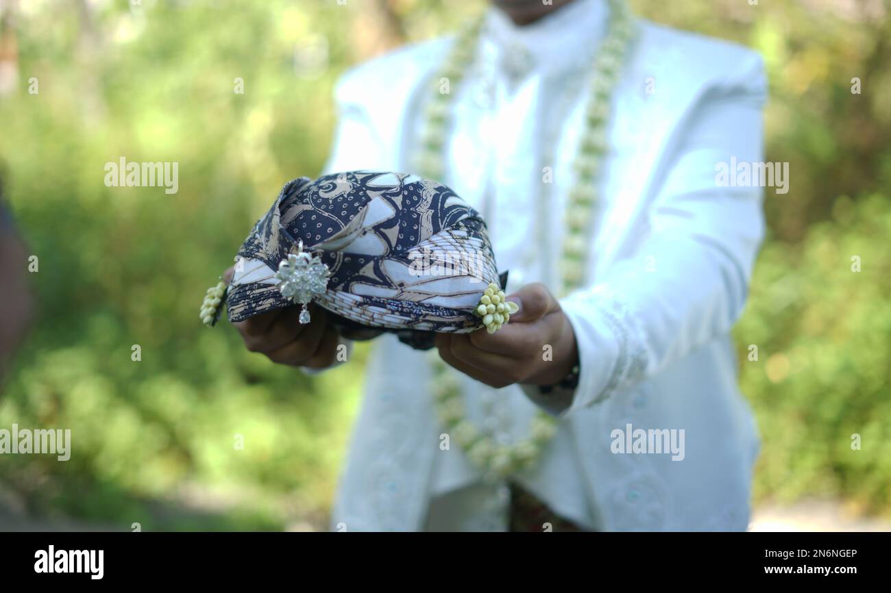 Sposo in abito da sposa tradizionale bianco che tiene tradizionale abito da testa Foto Stock