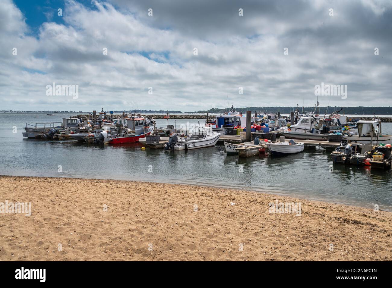 Una varietà di barche da pesca di diverse dimensioni ormeggiate a pontoni galleggianti a Poole Quay con acqua calma, in primo piano sabbioso, e piccole macchie di blu i. Foto Stock