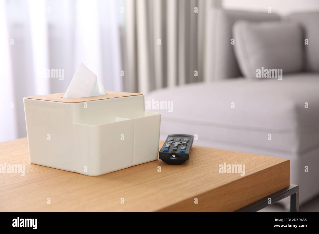 Box con fazzolettini di carta e telecomando TV su tavolo in legno nel soggiorno. Spazio per il testo Foto Stock