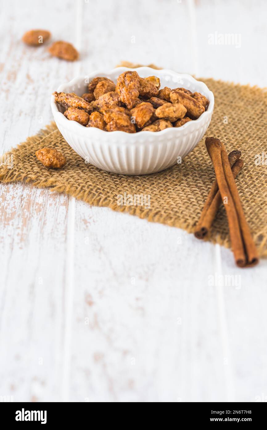 Ciotola di mandorle dolci candite su fondo bianco rustico in legno, verticale con spazio copia Foto Stock