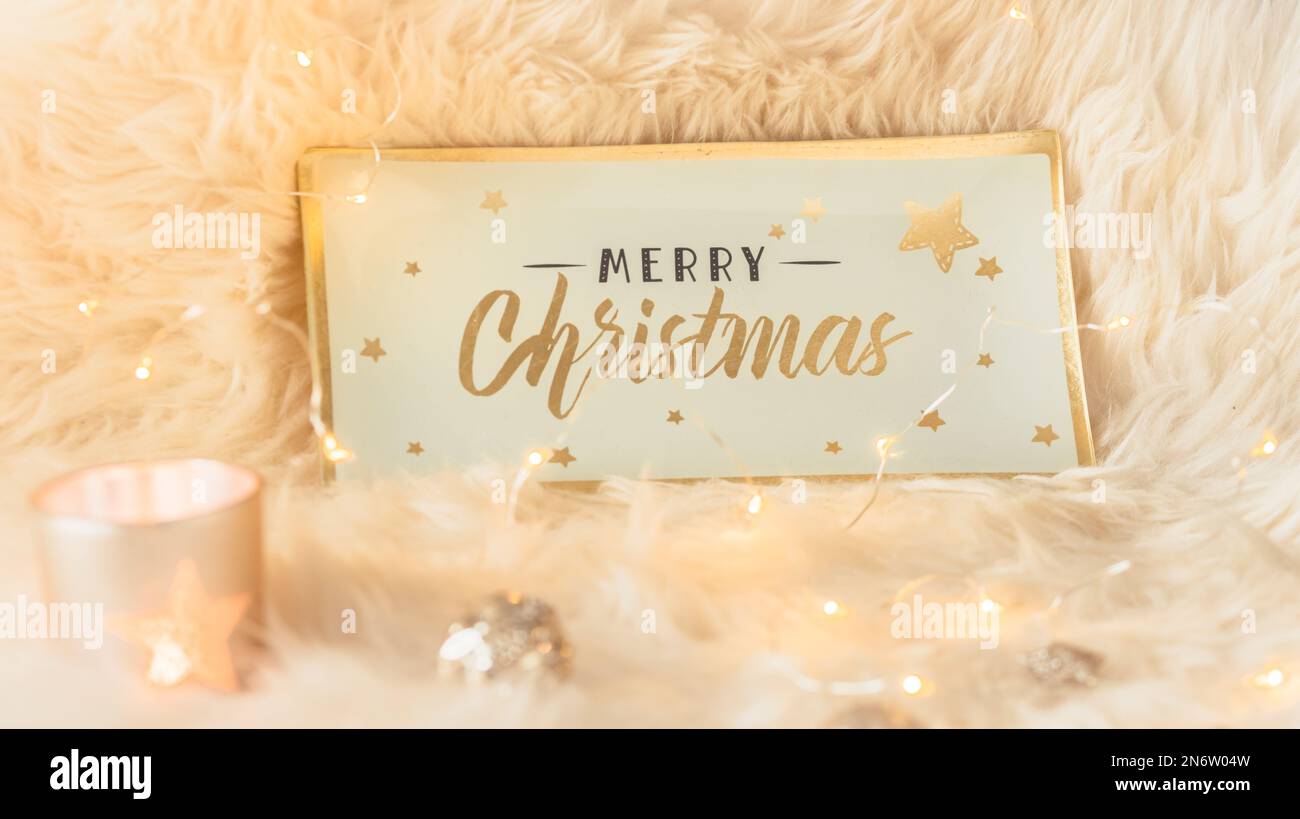 Allegra scritta di Natale su un segno di vetro o vassoio su una pelliccia bianca insieme con le decorazioni e le luci di Natale Foto Stock