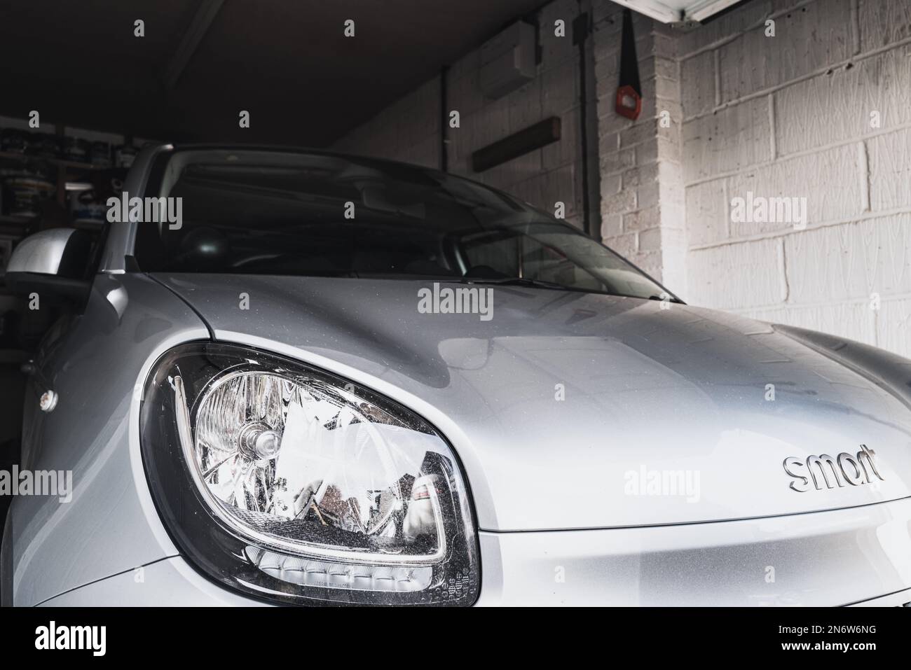 Poco a fuoco del marchio di un piccolo veicolo elettrico visto nel suo singolo garage. La vettura è attualmente in carica e pronta per un viaggio. Foto Stock