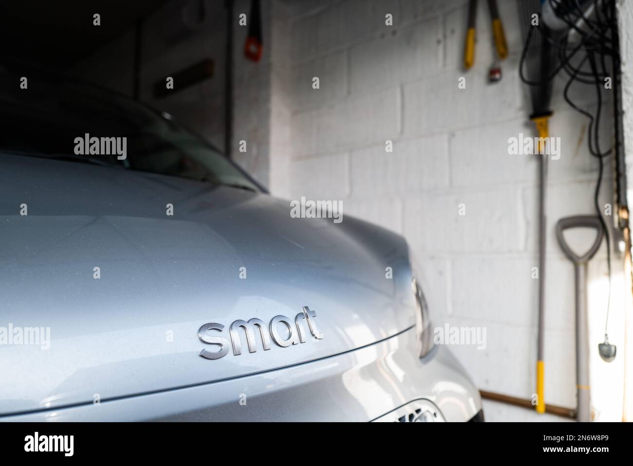 Poco a fuoco del marchio di un piccolo veicolo elettrico visto nel suo singolo garage. La vettura è attualmente in carica e pronta per un viaggio. Foto Stock