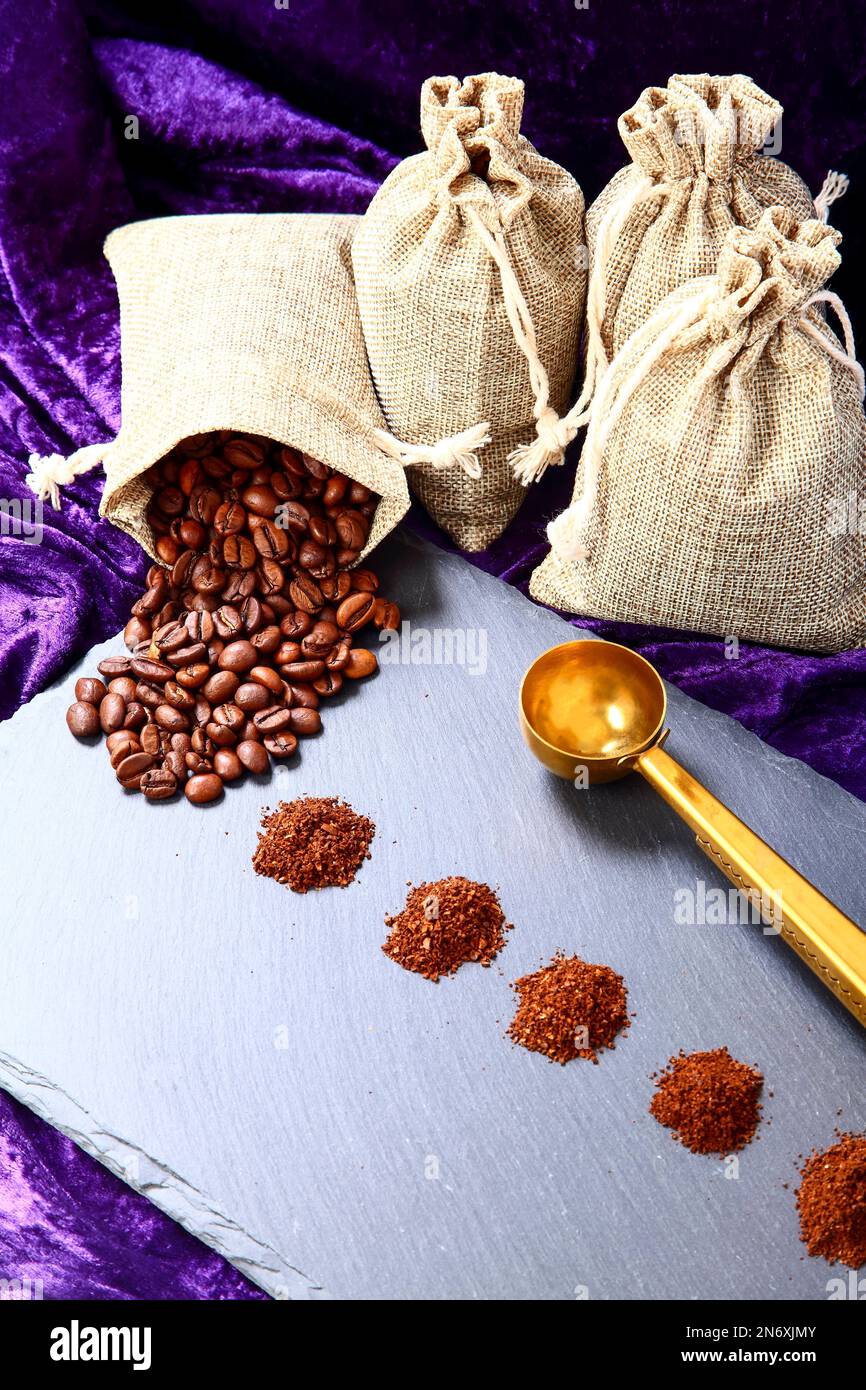 Sacchi di Hessian pieni di chicchi di caffè torrefatto con mucchi di caffè appena macinato Foto Stock