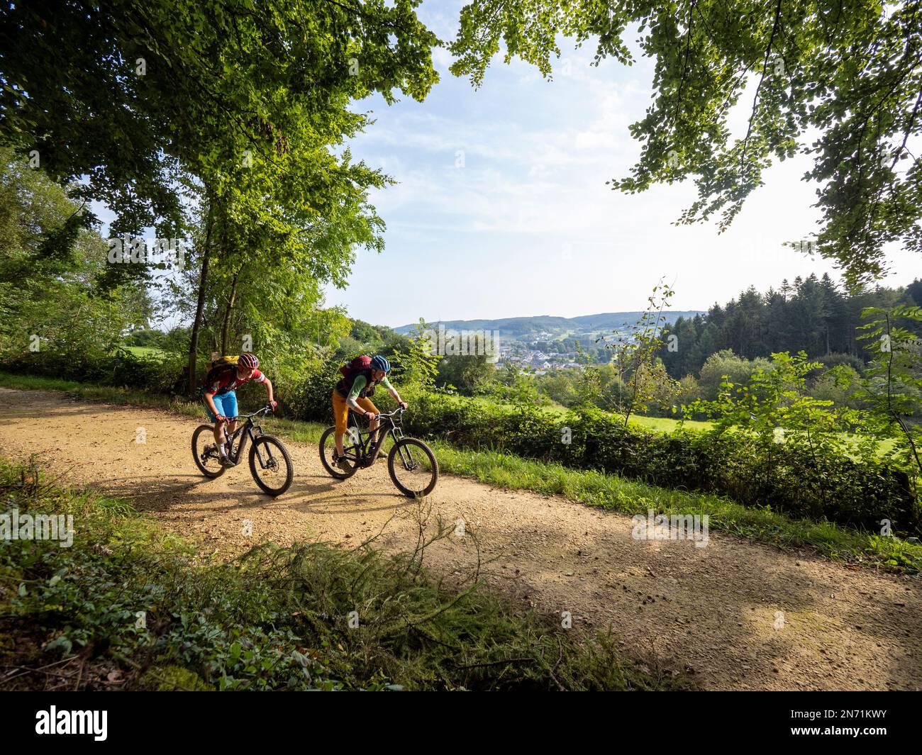 E-mountain biker su strada forestale in Lussemburgo. Città di Mersch sullo sfondo. Foto Stock