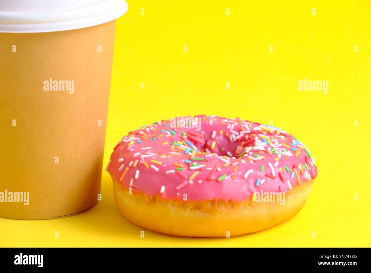 Tazza da caffè usa e getta e ciambella con sfondo giallo ghiaccio rosa Foto Stock