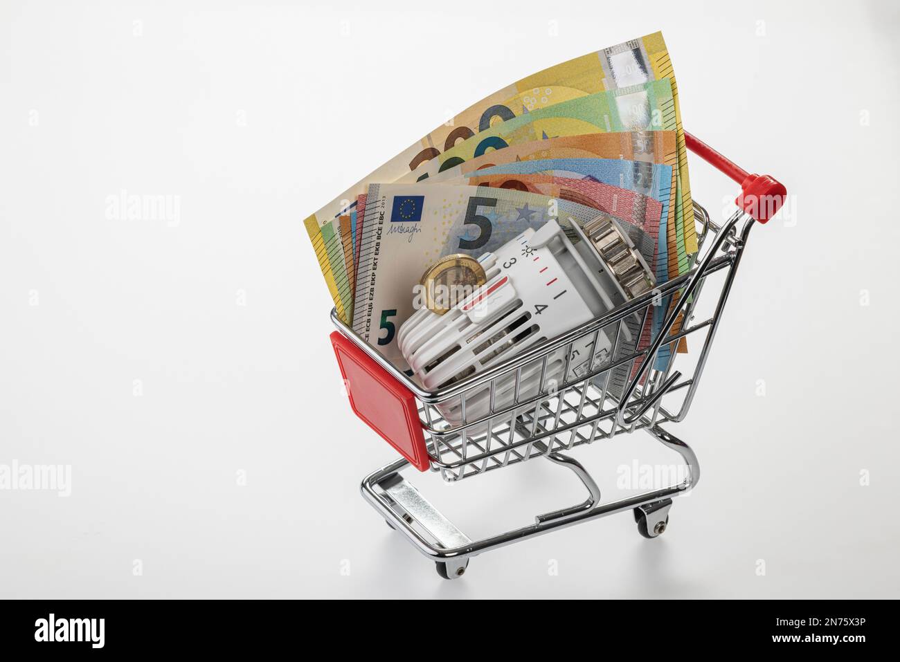 Carrello, banconote in euro, monete da 1 euro, termostato radiatore, immagine simbolo, acquisti, costi di energia, costi di riscaldamento crescenti, sfondo bianco, Foto Stock