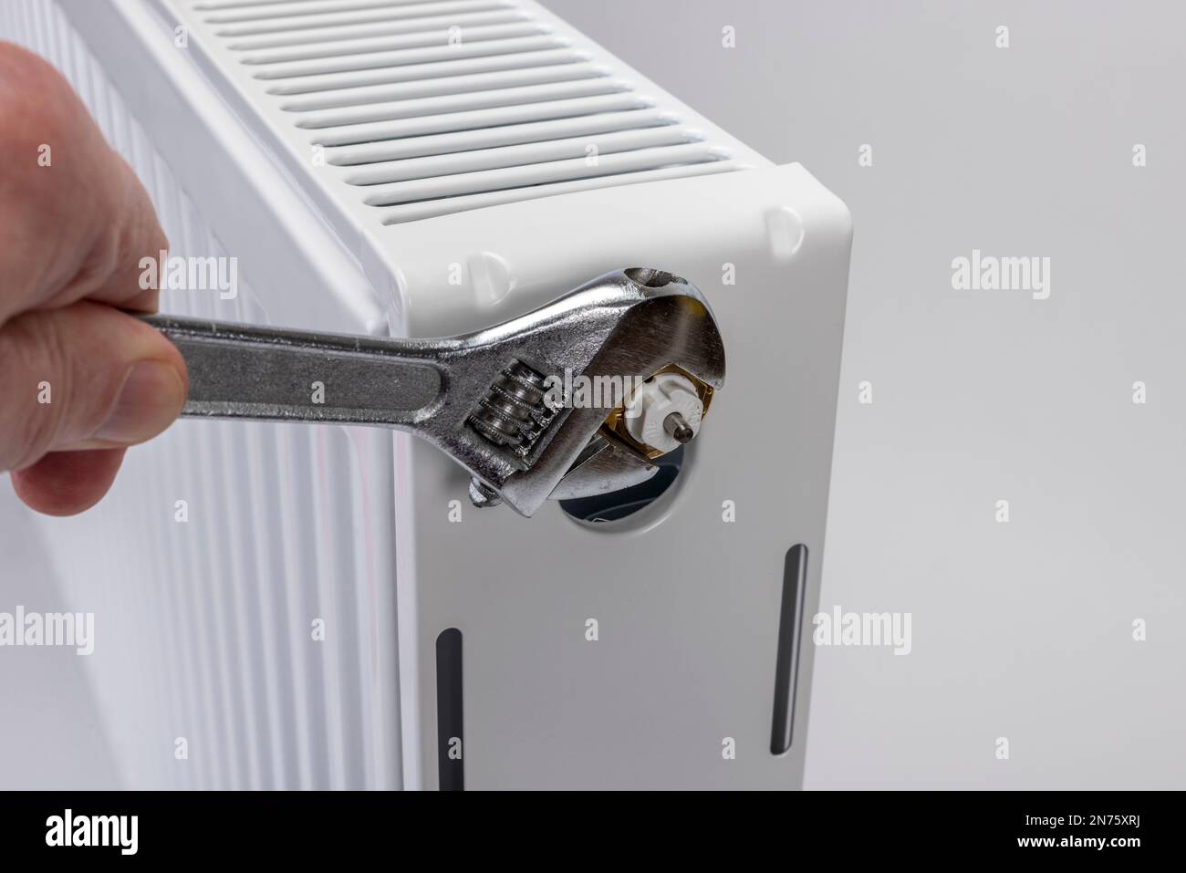 La mano dell'uomo con una chiave a forcella rotante allenta l'inserto della valvola del radiatore sul radiatore, sfondo bianco, immagine simbolo, inserto della valvola di ricambio, difettoso, Foto Stock