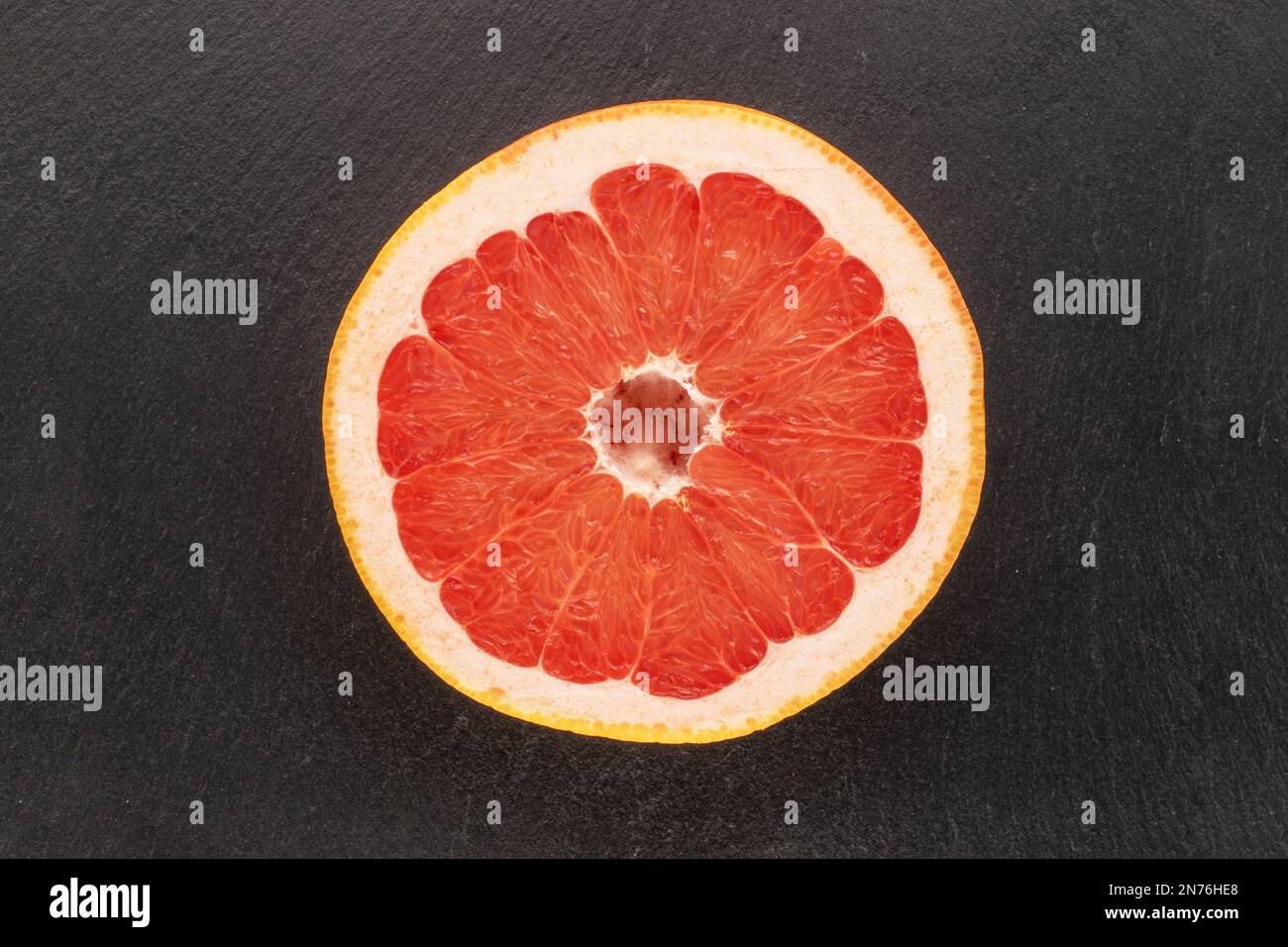 Una metà di pompelmo maturo su un piatto di ceramica nera, macro, vista dall'alto. Foto Stock