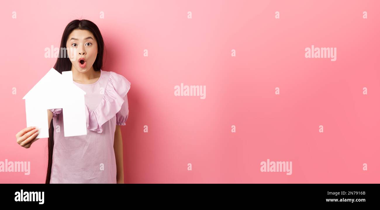 Concetto di immobili e assicurazioni. Entusiasta donna asiatica mostrando  taglio casa di carta e guardare stupito, offerta speciale, in piedi su  sfondo rosa Foto stock - Alamy