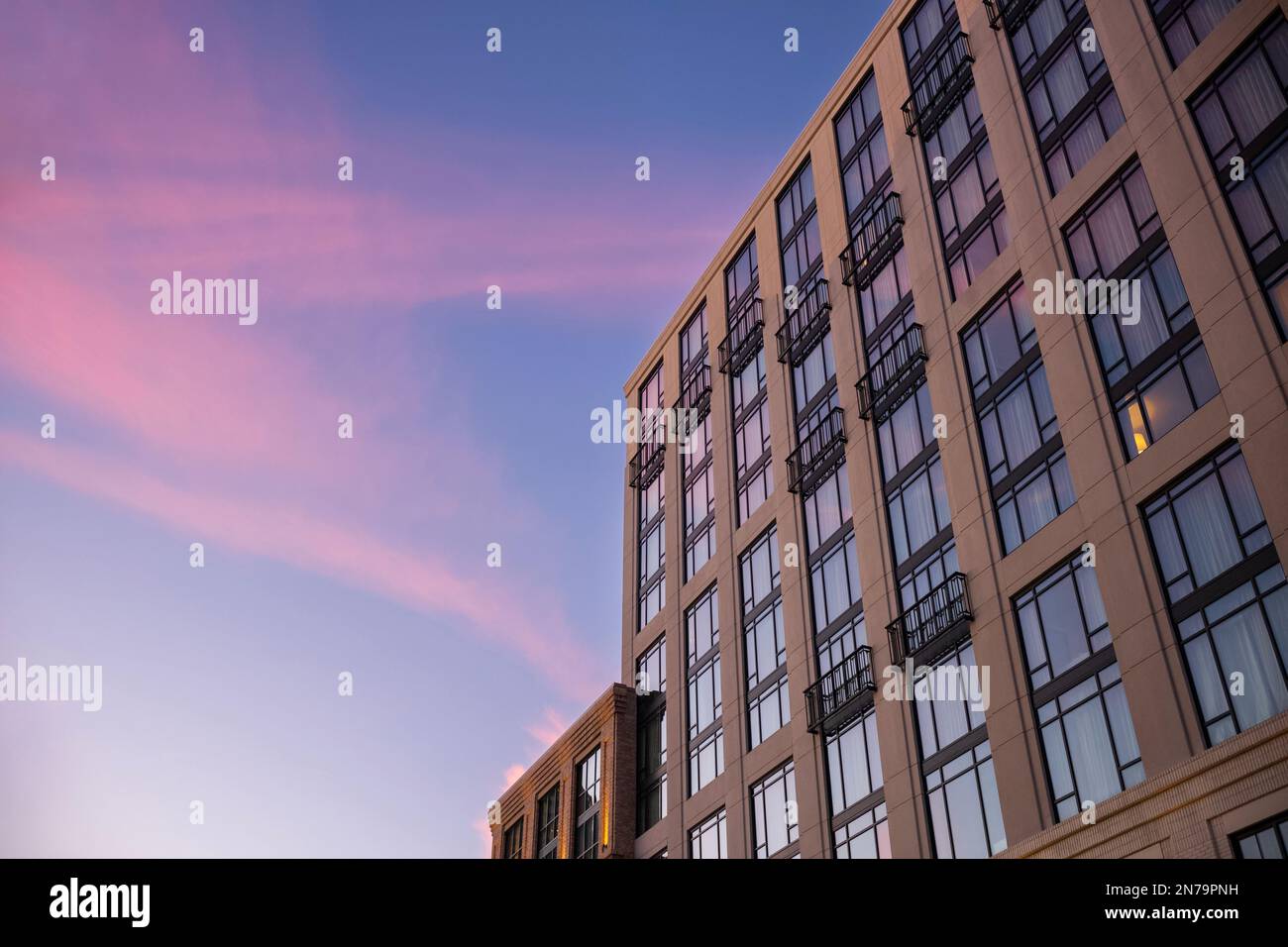 La facciata di un edificio con una stanza illuminata da una lampada da tavolo, fotografata al tramonto con un retrogusto delle nuvole sopra nel cielo. Foto Stock