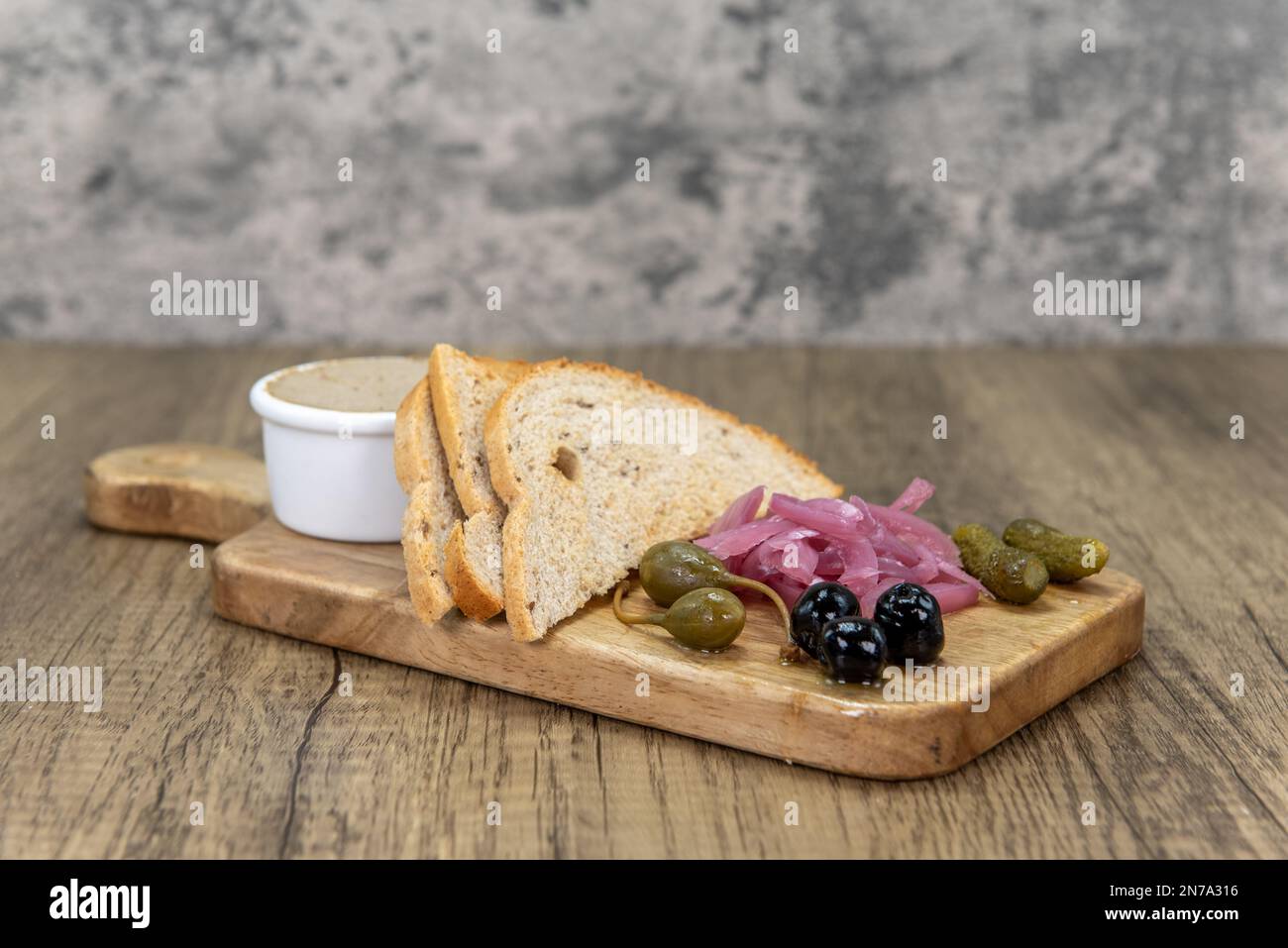 Appetitoso antipasto di pate' con cornichon e bacche di cappero servite su un tagliere di legno. Foto Stock