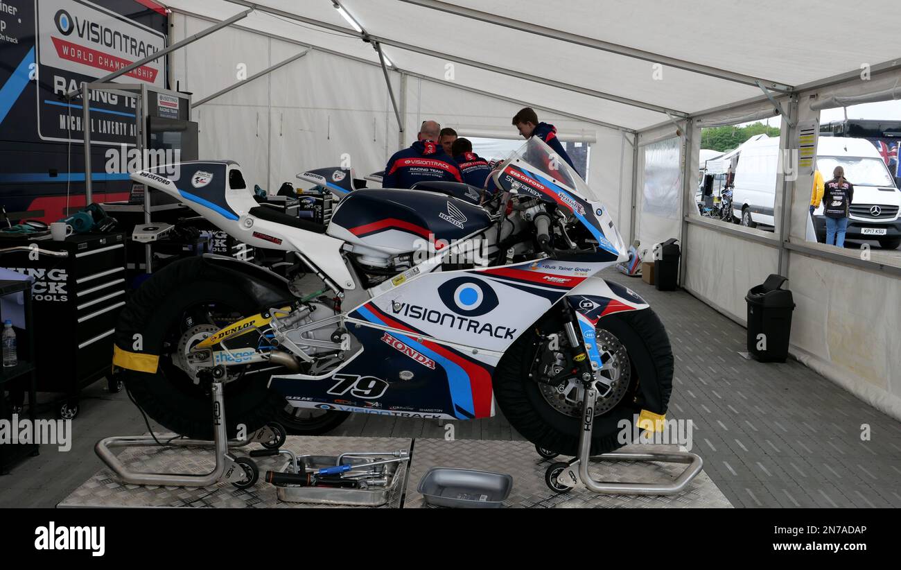 Moto da corsa che vengono revisionate e preparate da meccanici sotto un tendone in un paddock di gara. Foto Stock