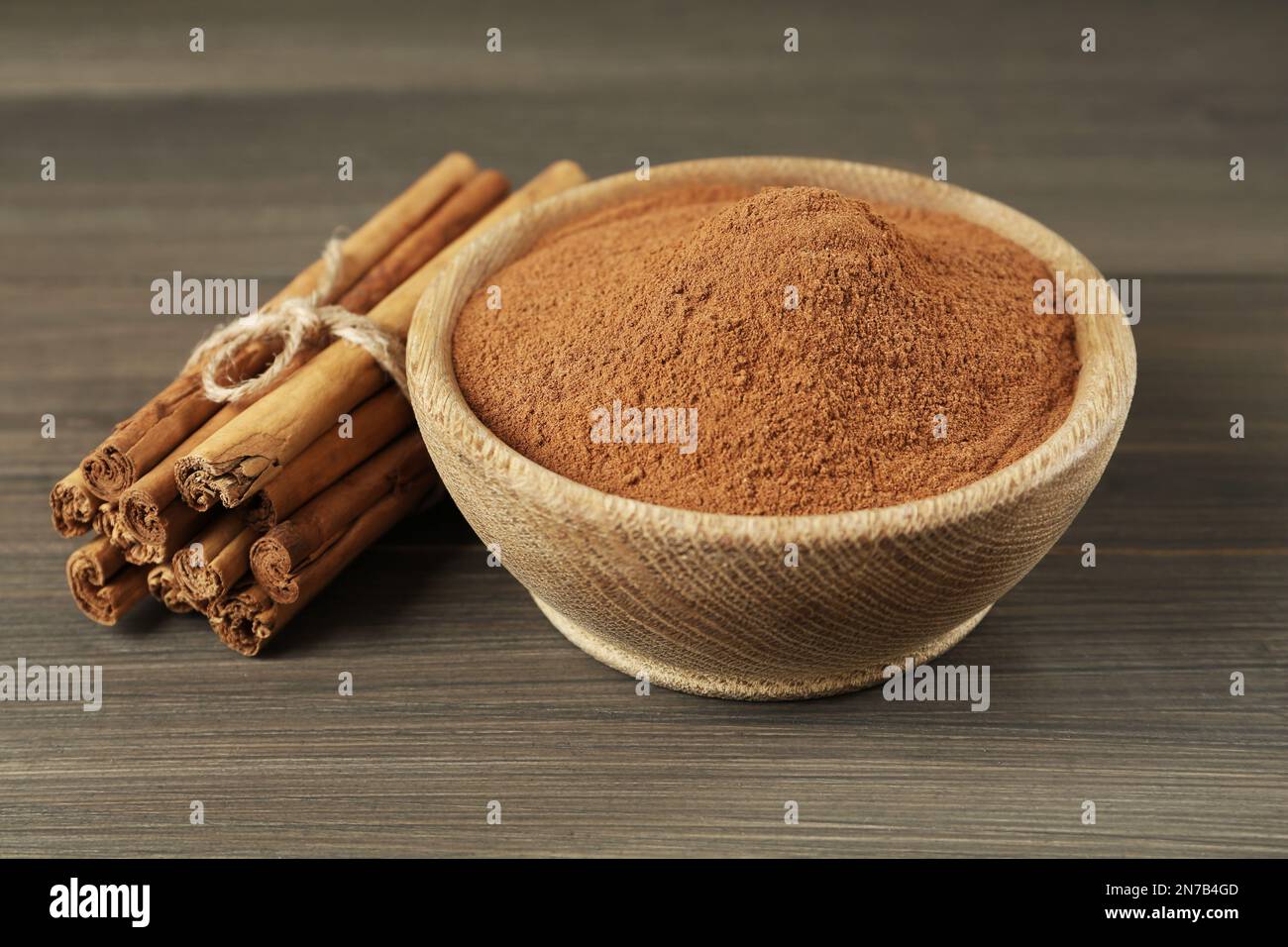 Cannella in polvere aromatica in ciotola e bastoncini su tavola di legno Foto Stock