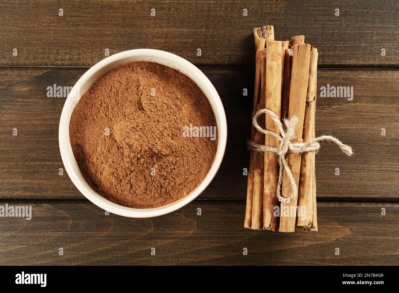 Cannella in polvere aromatica in ciotola e bastoni su tavola di legno, piatto Foto Stock