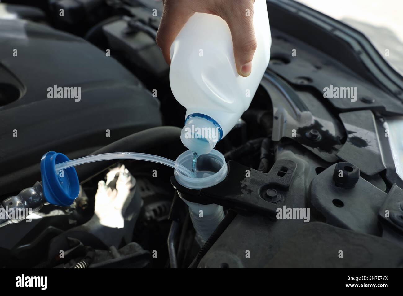 Man che versa l'antigelo dal contenitore in plastica nel serbatoio del liquido lavacristalli, fare un primo piano Foto Stock