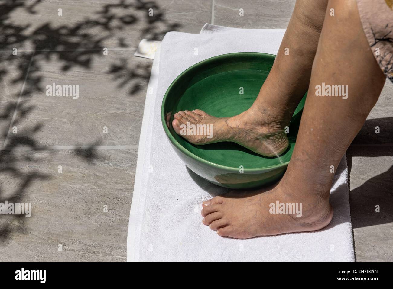 Donna anziana che si immergi i piedi con acqua salata calda a casa. Foto Stock