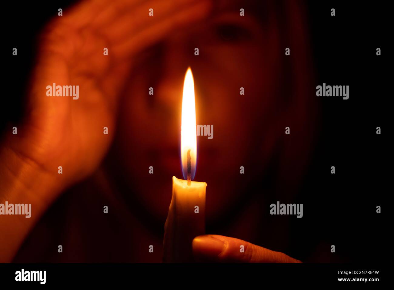 ragazza sullo sfondo di una candela bruciante in preghiera al buio Foto Stock