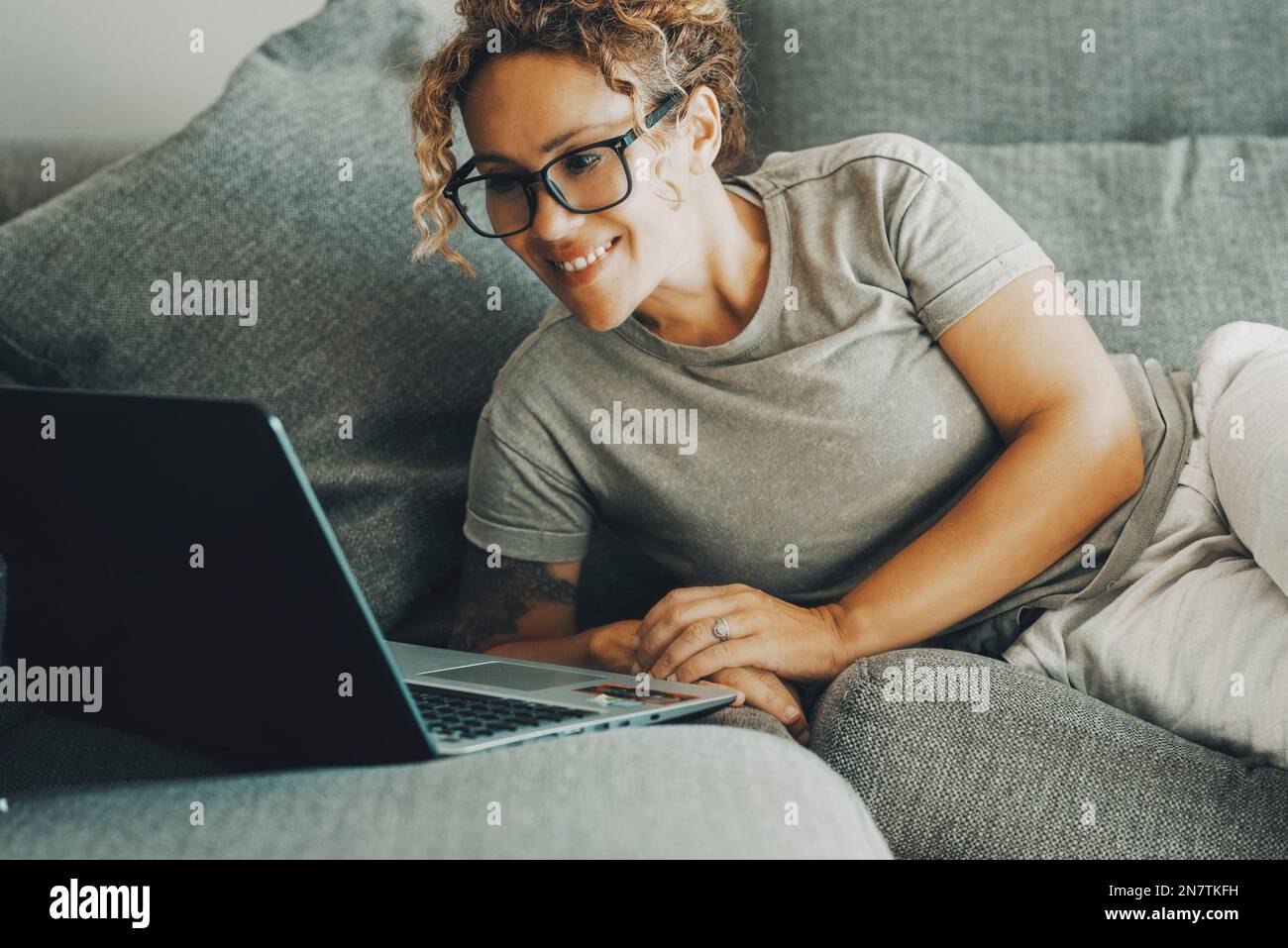 Giovane donna caucasica sdraiata sul divano in soggiorno lavoro online su laptop gadget. Donna Millennial relax riposo sul divano a casa guardare lo schermo del computer Foto Stock