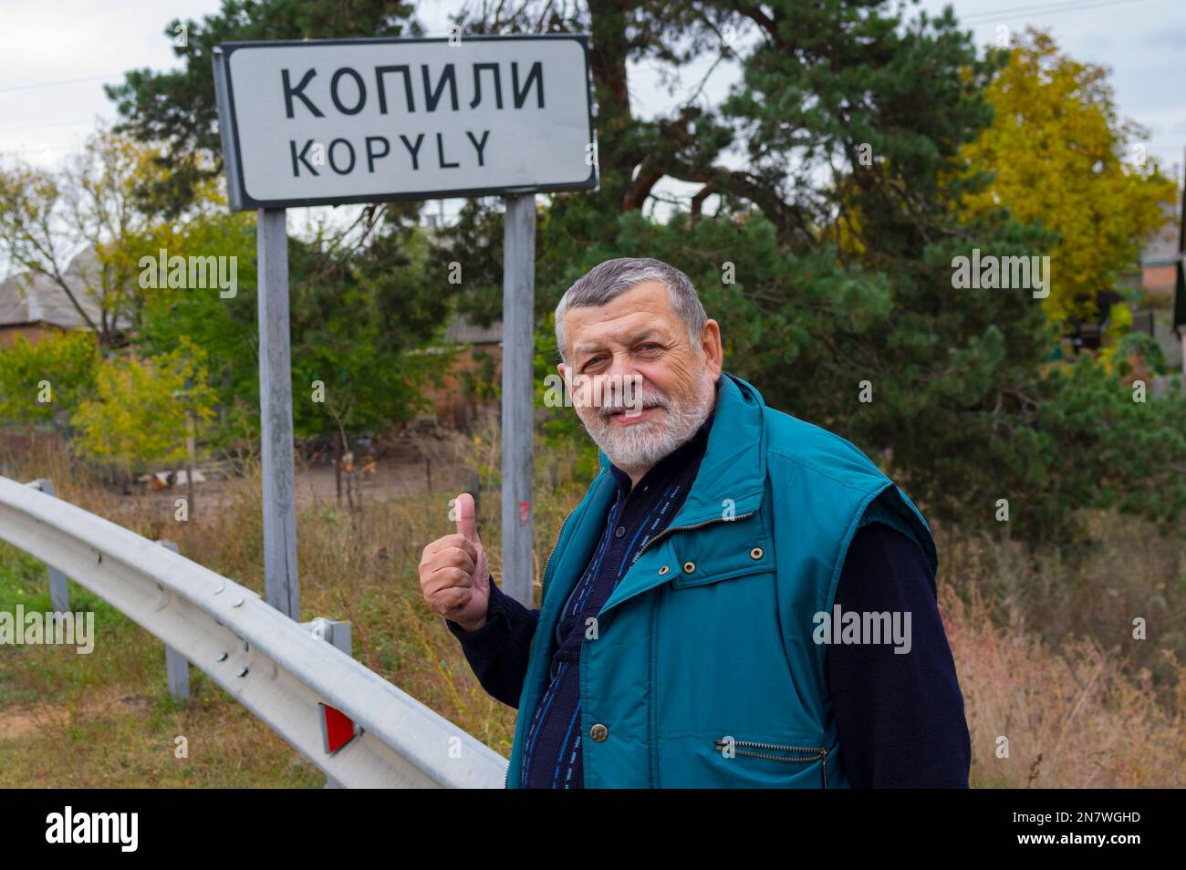 Ritratto di UkrinianSenior positivo in piedi sulla strada Kharkiv-poltava nuovo segno che segna Kopyly villaggio, Ucraina Foto Stock