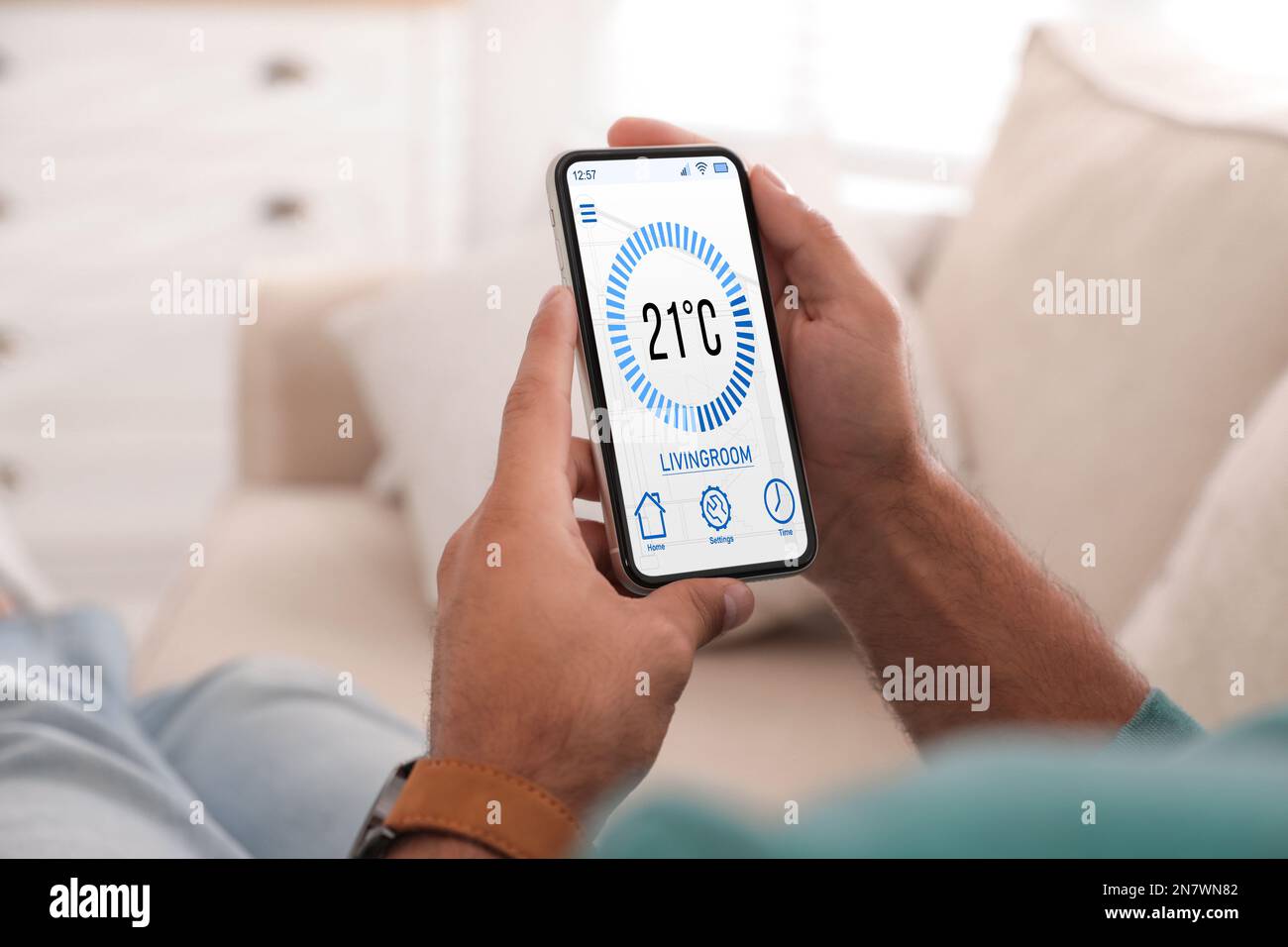 Uomo che utilizza lo smartphone per controllare l'impianto di riscaldamento in casa, in primo piano Foto Stock