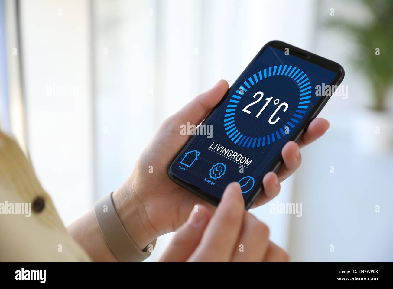 Uomo che utilizza lo smartphone per controllare l'impianto di riscaldamento in casa, in primo piano Foto Stock