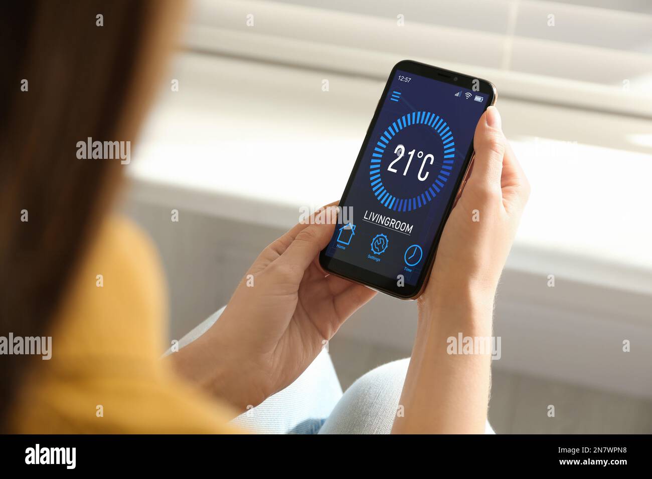 Donna che utilizza lo smartphone per controllare il sistema di riscaldamento in casa, in primo piano Foto Stock