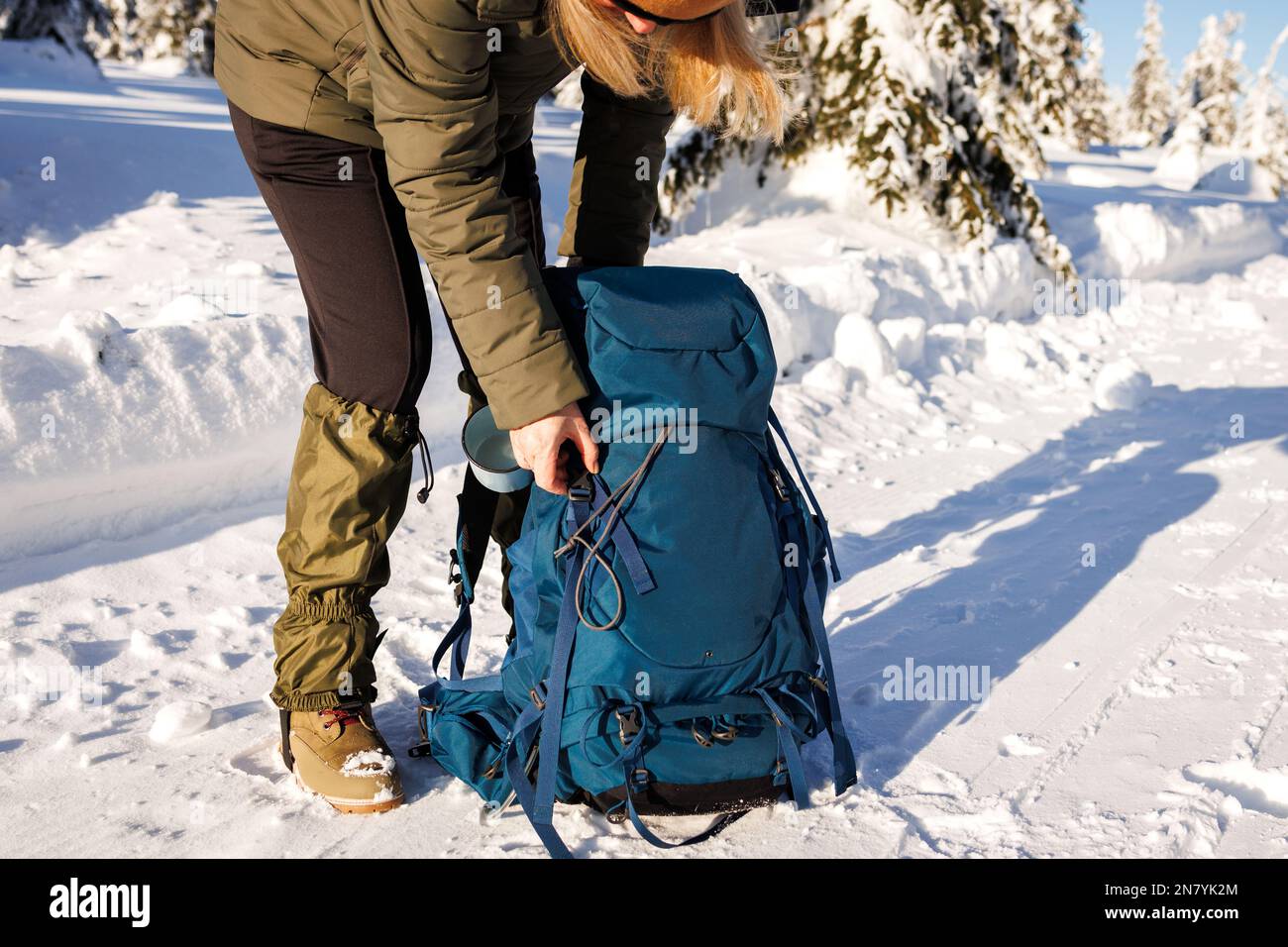 Donna che apre lo zaino durante il riposo durante il trekking invernale. Escursioni nella natura innevata. Attrezzature sportive Foto Stock
