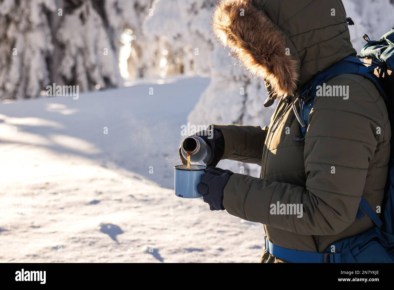 Escursionista che versa la bevanda calda dai thermos nella tazza da viaggio. Rinfresco durante il trekking invernale nelle giornate fredde Foto Stock