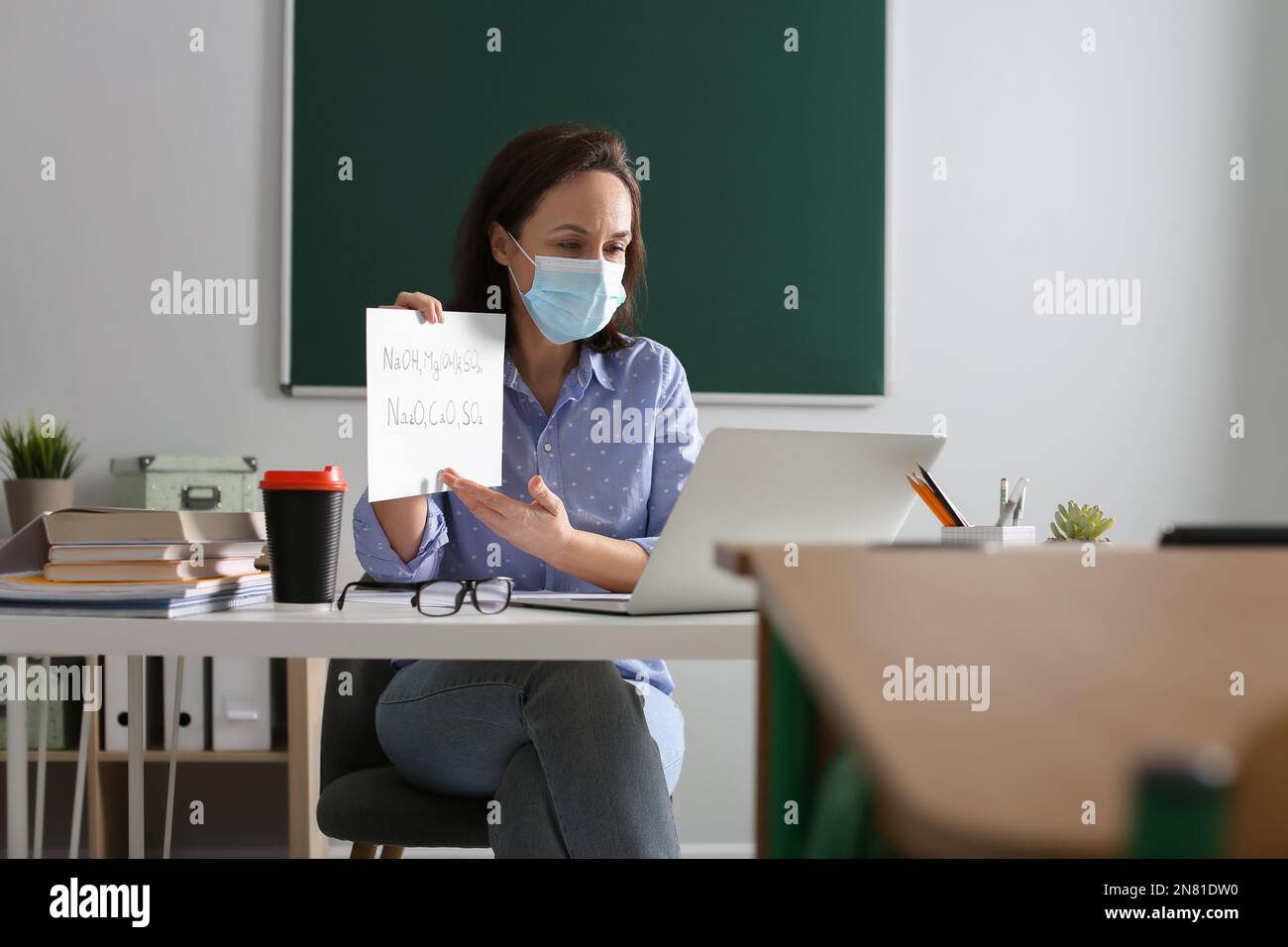 Insegnante con maschera protettiva che conduce una lezione online in aula durante la quarantena COVID-19 Foto Stock