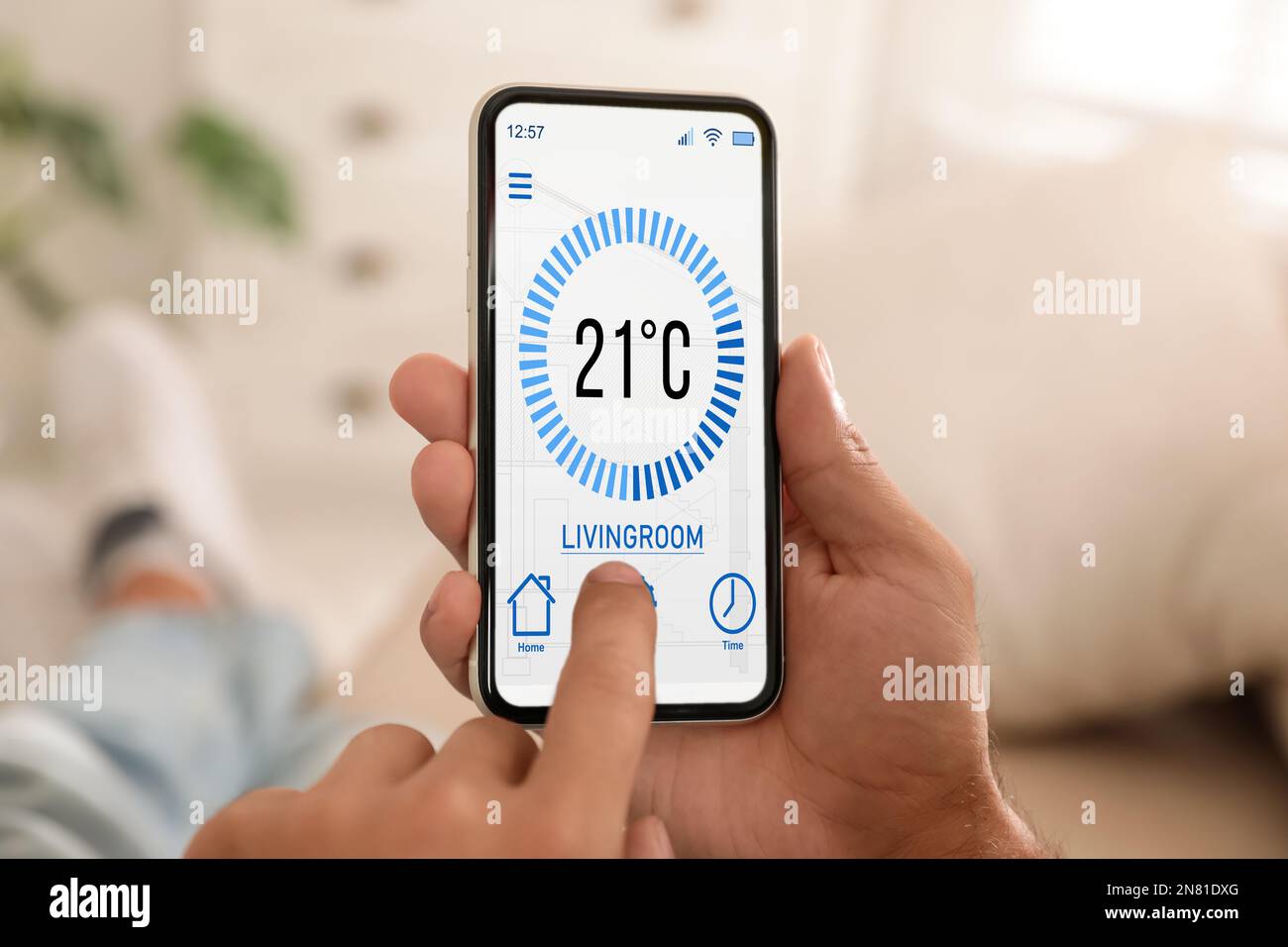 Uomo che utilizza lo smartphone per controllare l'impianto di riscaldamento in casa, in primo piano Foto Stock