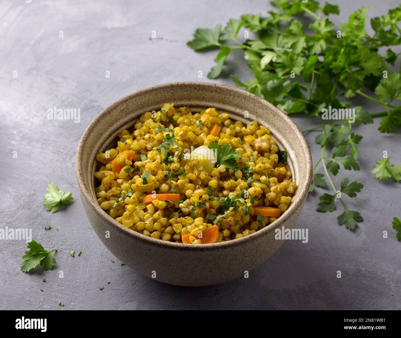 Sana ciotola di cibo fatta in casa con grano saraceno verde, verdure (cipolle, carote, aglio), verdi e curry con un bicchiere d'acqua sul dorso grigio testurizzato Foto Stock