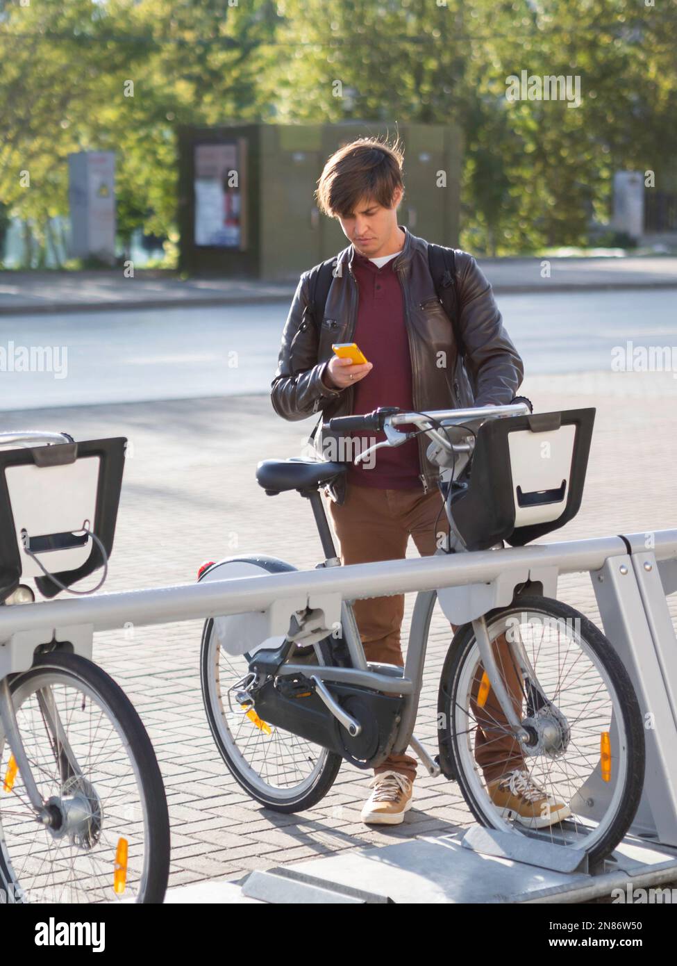 Il giovane uomo sta noleggiando una bicicletta per applicazione smartphone. Trasporto urbano ecologico in affitto. Stile di vita sano nella città moderna. Tramonto autunnale. Foto Stock
