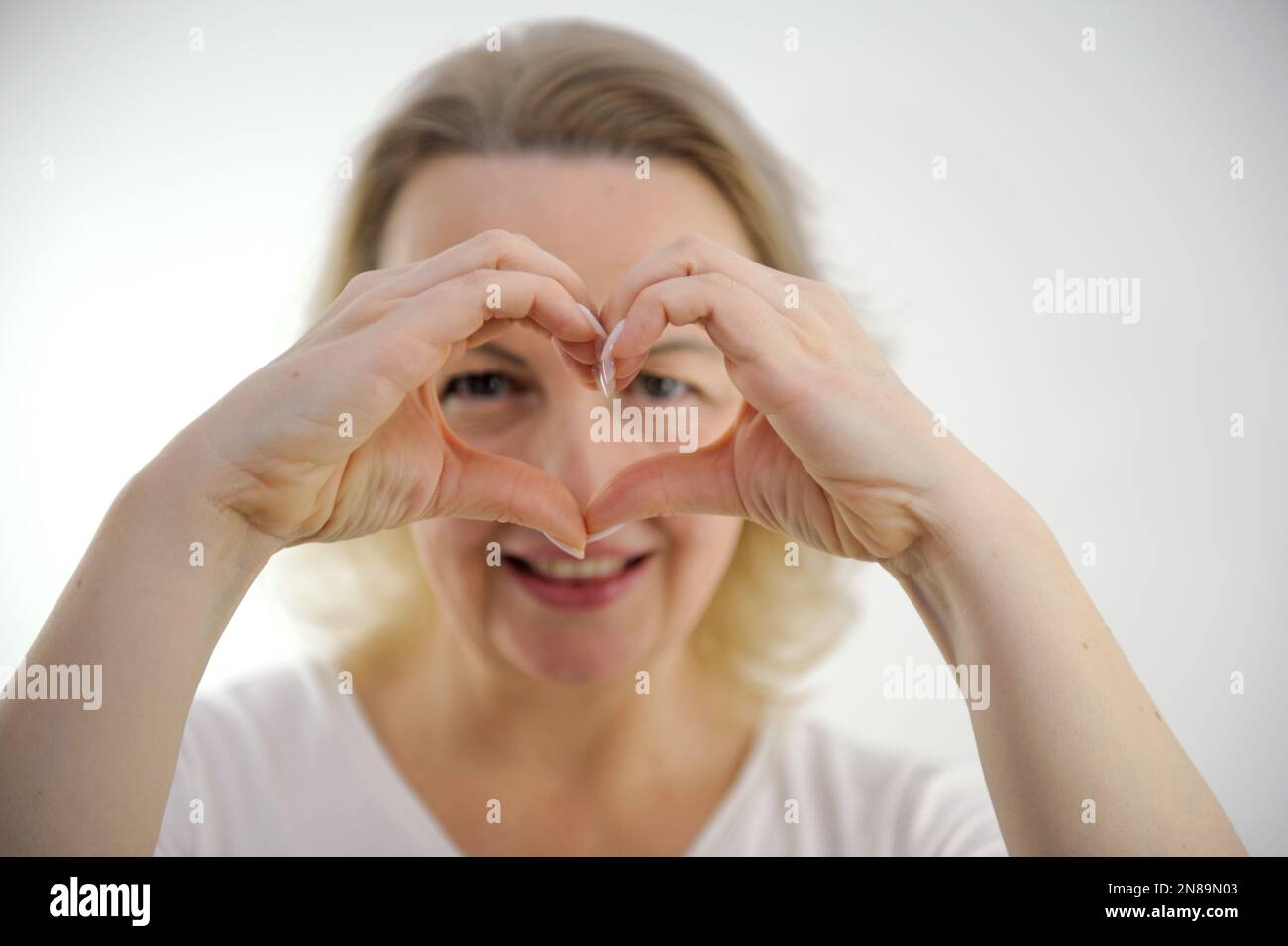 donna di mezza età fa le mani come se gli occhiali di fronte agli occhi che mostrano il cuore con le mani guarda attraverso il foro sorrisi amore aspettative riconoscimento tenerezza mani di bellezza in nitidezza selettiva nitidezza Foto Stock