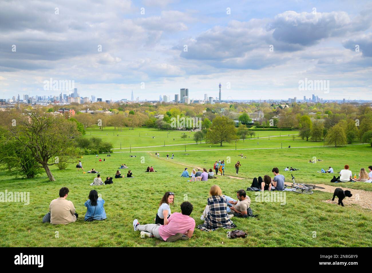 Persone che si rilassano sulle pendici erbose del parco Primrose Hill con vedute ininterrotte dei famosi edifici sullo skyline di Londra, North London England UK Foto Stock