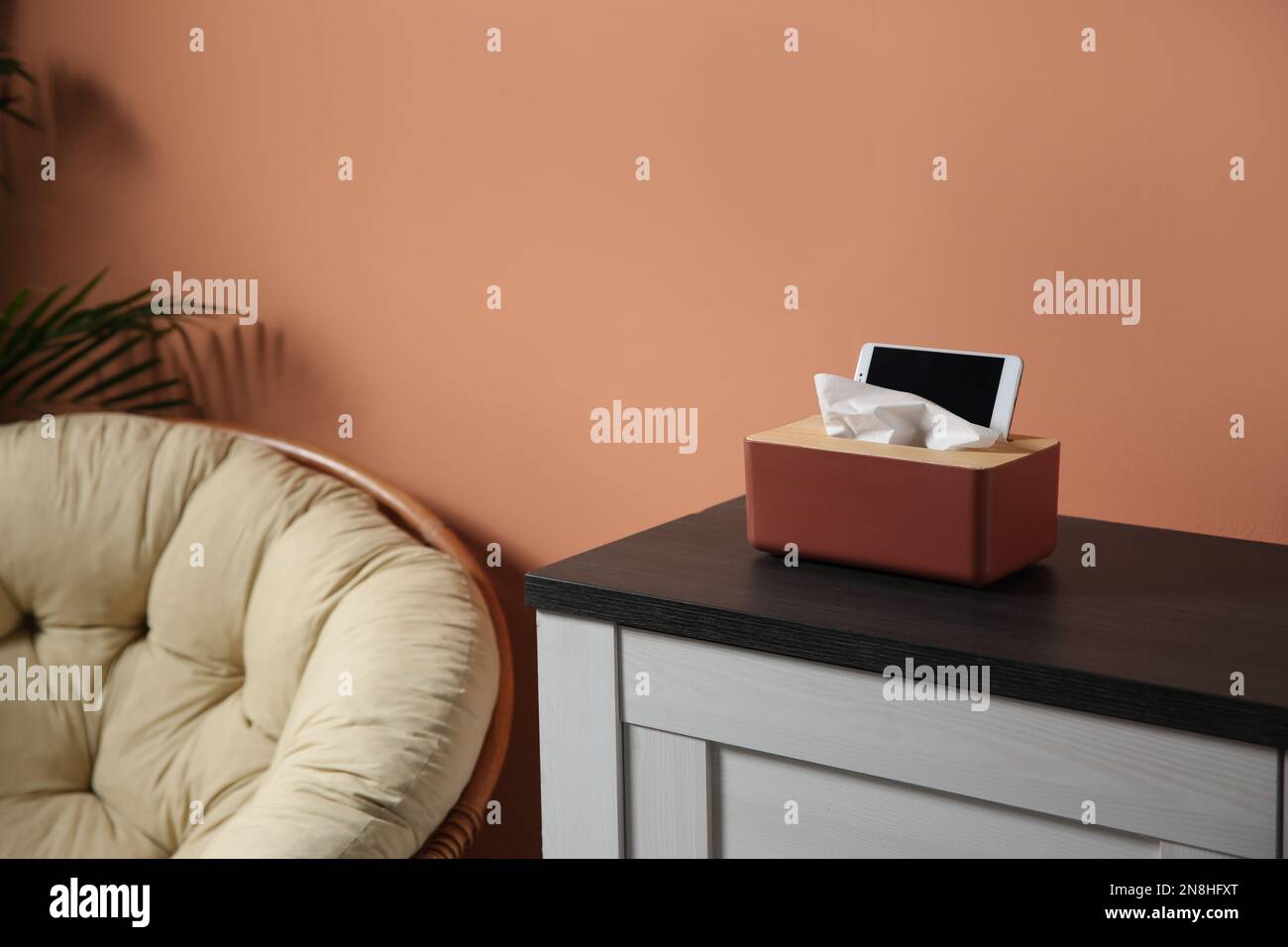 Scatola con fazzolettini di carta e smartphone su armadietto di legno in camera Foto Stock