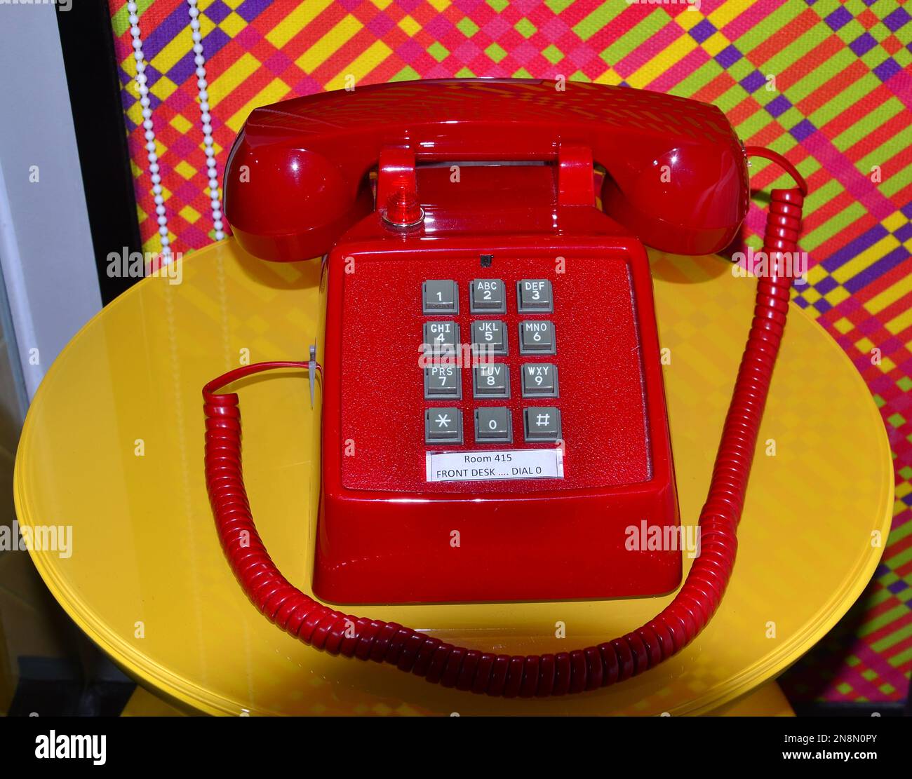 Un telefono o un telefono rosso brillante con pulsanti su un tavolo giallo luminoso Foto Stock