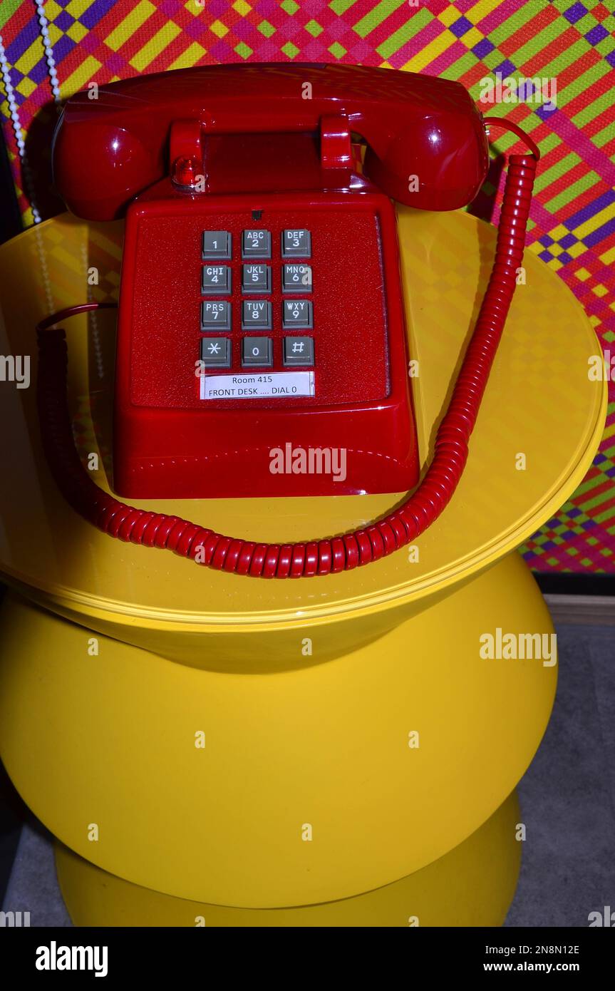 Un telefono o un telefono rosso brillante con pulsanti su un tavolo giallo luminoso Foto Stock