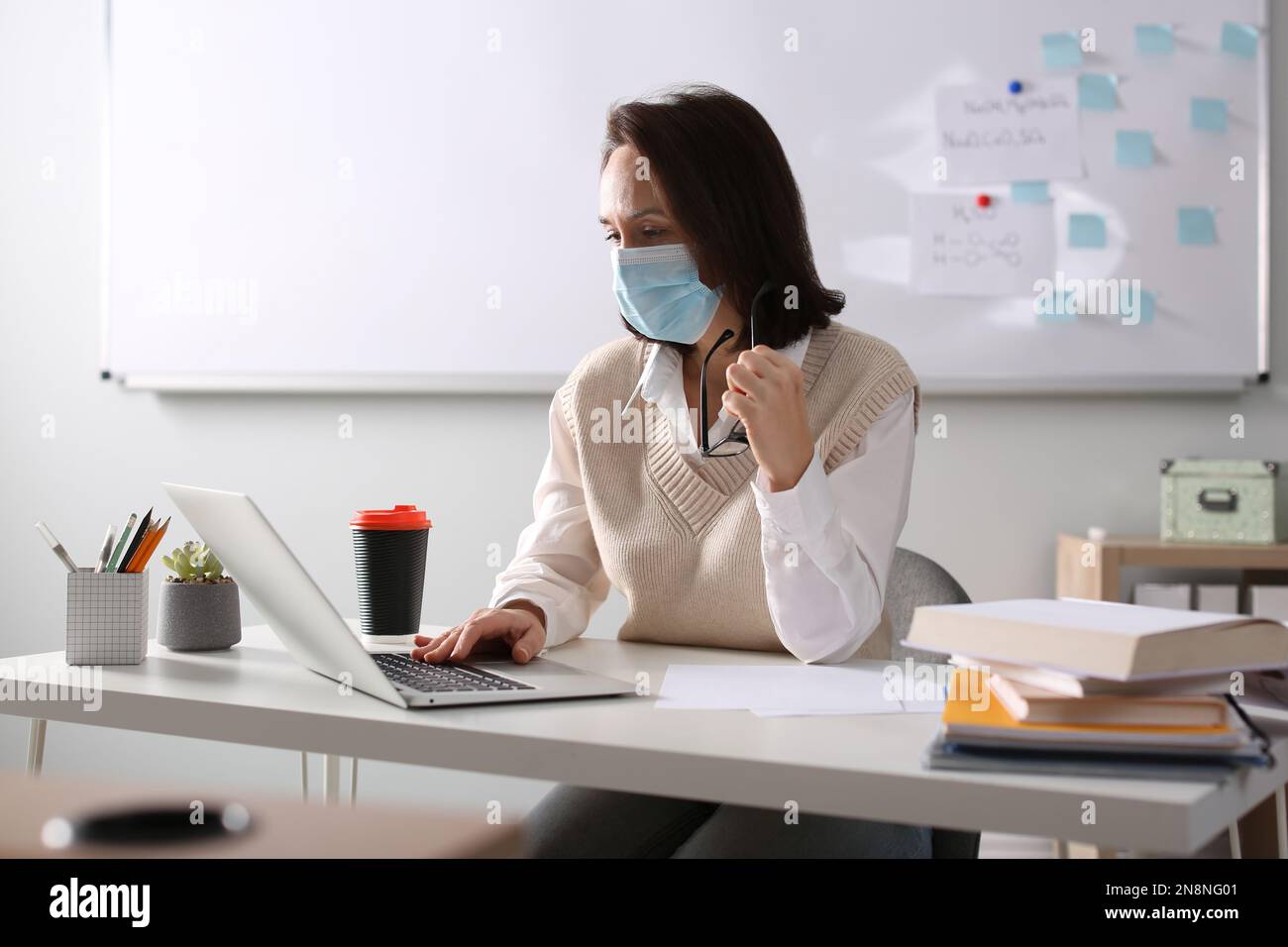 Insegnante con maschera protettiva che conduce una lezione online in aula durante la quarantena COVID-19 Foto Stock