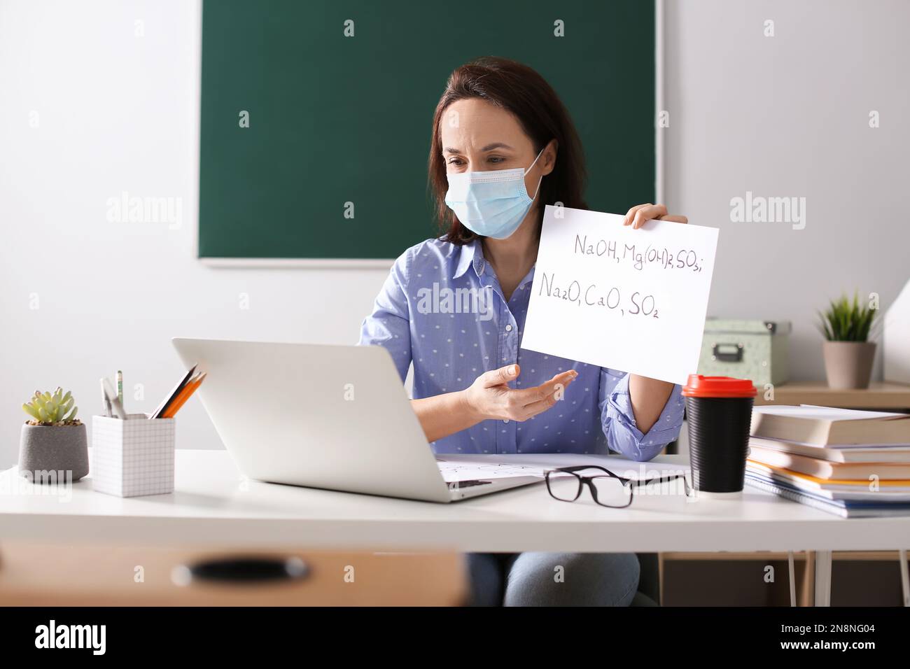 Insegnante con maschera protettiva che conduce una lezione online in aula durante la quarantena COVID-19 Foto Stock