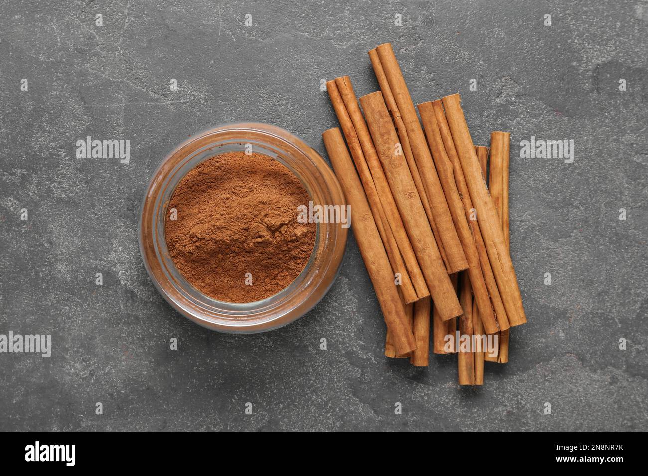 Cannella in polvere aromatica e bastoncini su tavola grigia, a giacitura piatta Foto Stock