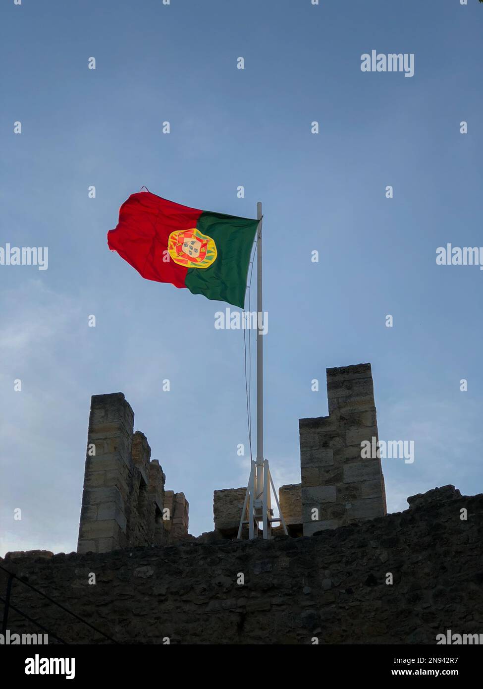 Una foto verticale della bandiera portoghese che sventola sul Castello di San Giorgio a Lisbona, Portogallo Foto Stock