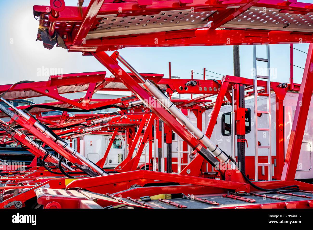 Trasporti di automobili standard industriali semirimorchi grandi bianchi classici con semirimorchi modulari idraulici vuoti di colore rosso brillante in piedi sul pa industriale Foto Stock